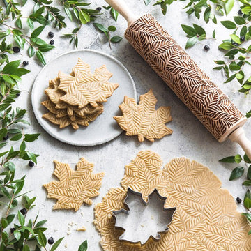Leaves pattern engraved on a wooden embossed rolling pin, beside the shortbread cookies it prints