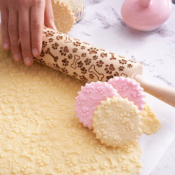 Paws pattern engraved on a wooden embossed rolling pin, beside the shortbread cookies it prints