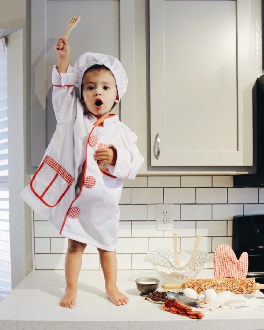 Karolina's young son in a chef's hat and apron, standing on the kitchen counter next to a rolling pin